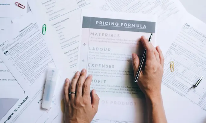 Human hands working on a spread of work papers on a desk focused on pricing.