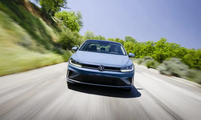 Front view of a powder blue 2025 Volkswagen Jetta driving down a road during the day.