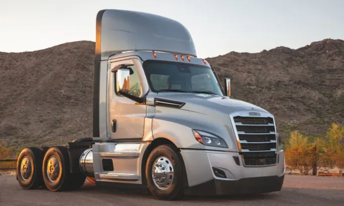 A day cab semi-tractor parked in a roadway in front of a desert mountain ridge at sunset.