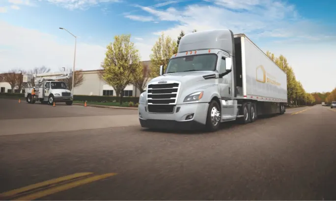 A white day cab semi driving past a regional trucking distribution center.