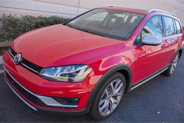 A red 2017 VW Golf Alltrack SEL sits on a road in front of a buliding.