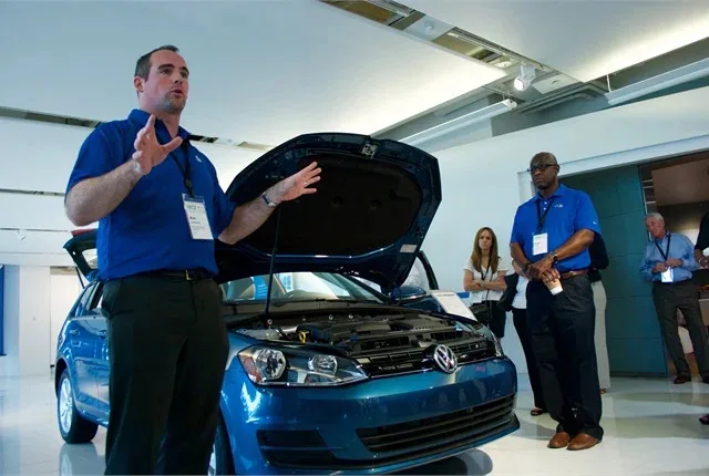 VW employees stand in front of a blue 2017 Golf Sportwagen 4Motion as they explain a new product.
