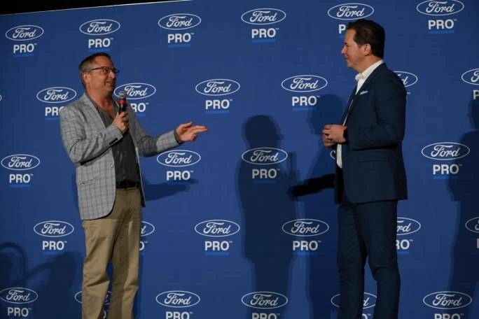 Chris Brown of Bobit/Fleet Group speaks into a microphone while standing on stage with Matt Atkenson of Ford Pro in front of a Ford Pro branded backdrop at Work Truck Week.