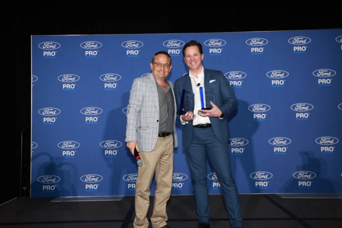 Chris Brown, associate publisher at Bobit/Fleet Group, stands with Matt Atkenson of Ford Pro as Atkenson holds two Commercial Van of the Year awards in front of a Ford Pro backdrop at Work Truck Week.
