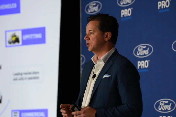 Matt Atkenson, executive director of Ford Pro North American Sales and Operations, speaks on stage during a presentation at Work Truck Week with a Ford Pro branded backdrop behind him.