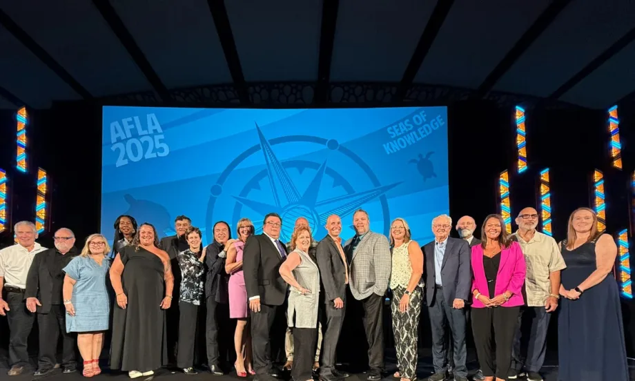 A group of AFLA award winners stand on a stage in front of a blue background with AFLA on the front.