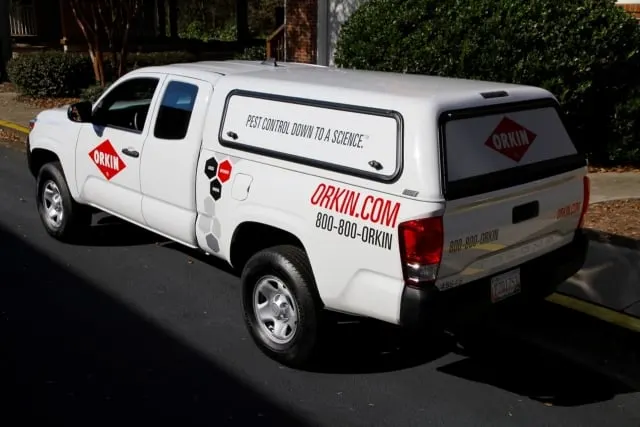 White Orkin-branded Toyota Tacoma service truck with a covered bed parked along a curb.