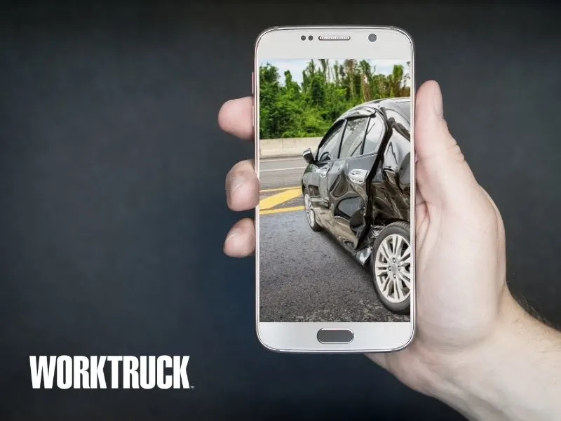 Person holding a cellphone with an image on the screen of a car that has been involved in a collision.
