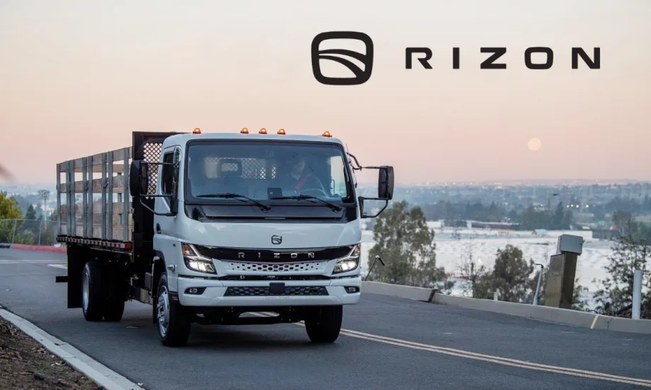 Stake body medium-duty electric truck driving on a road with sunset in background and Rizon logo upper right against sky.