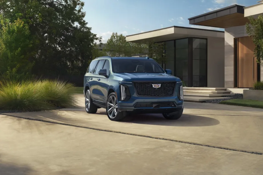 Sunny outdoor shot of a blue 2025 Cadillac Escalade SUV in the drive way of a house.