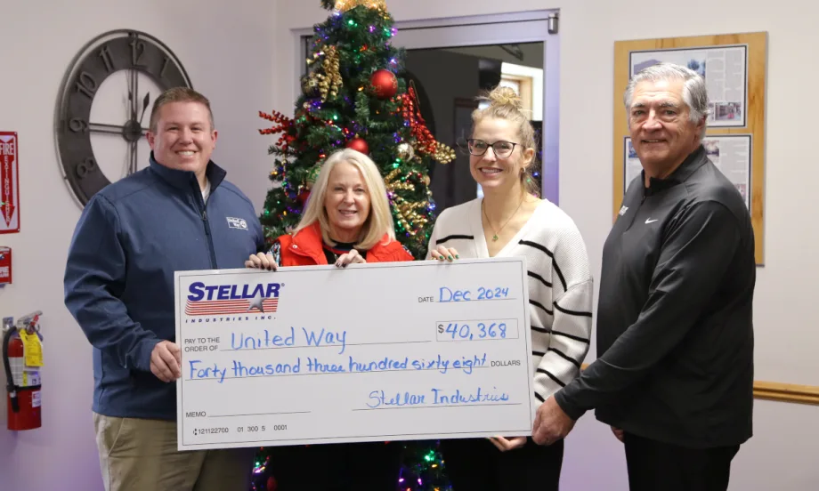 Four business people hold a large symbolic check as part of a charitable donation.
