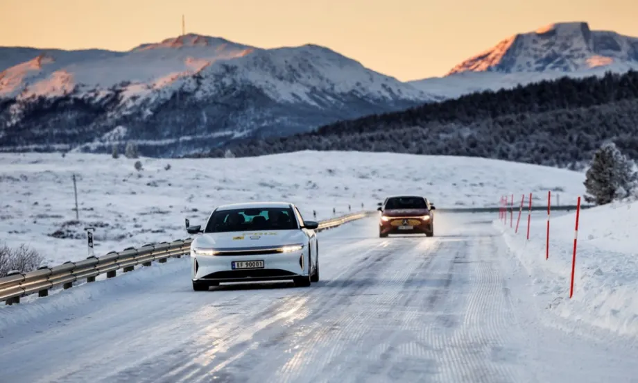 A Lucid Air Grand Touring drives on a snow-covered road in Norway during the NAF Winter Test, with mountains in the background and winter conditions visible.