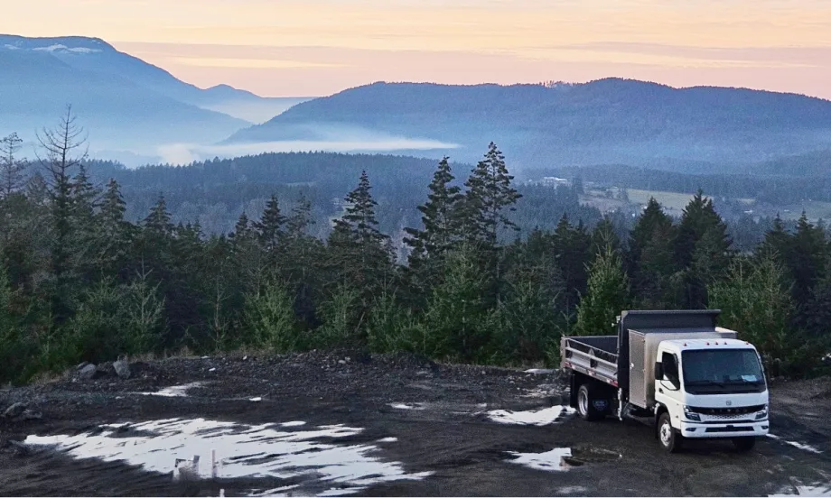 Electric truck parked in front of a scenic mountain background.