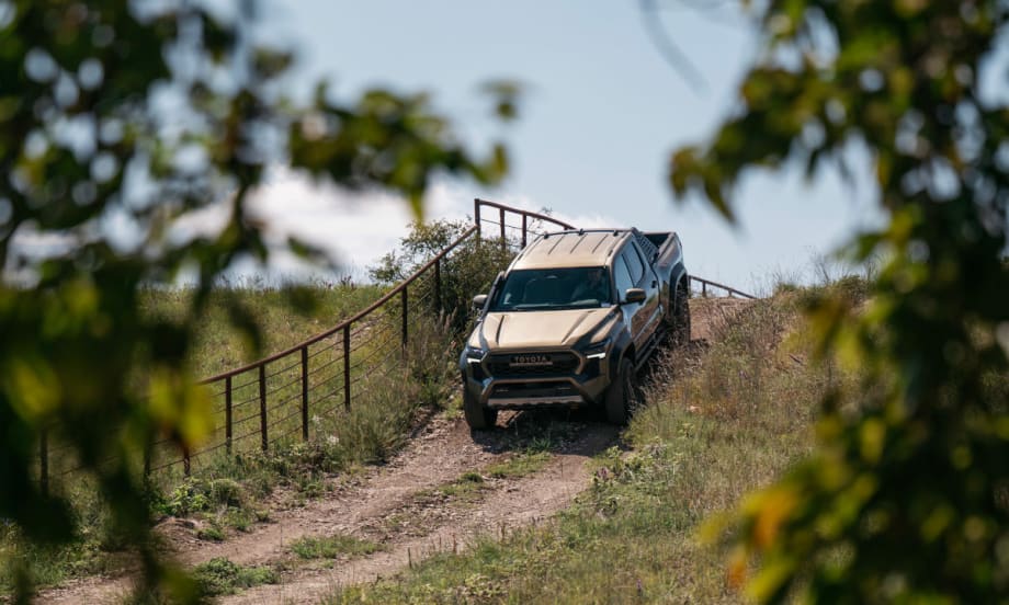 View through trees of a pickup truck cresting a hill in a farm setting.