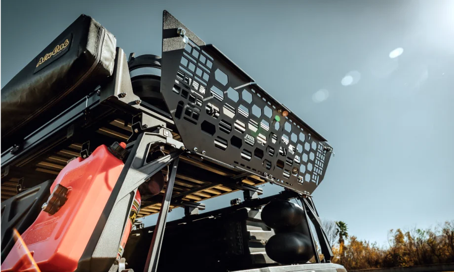 metal gate locks the area above the tailgate of a pickup truck. Photo shows it open against a blue sky.