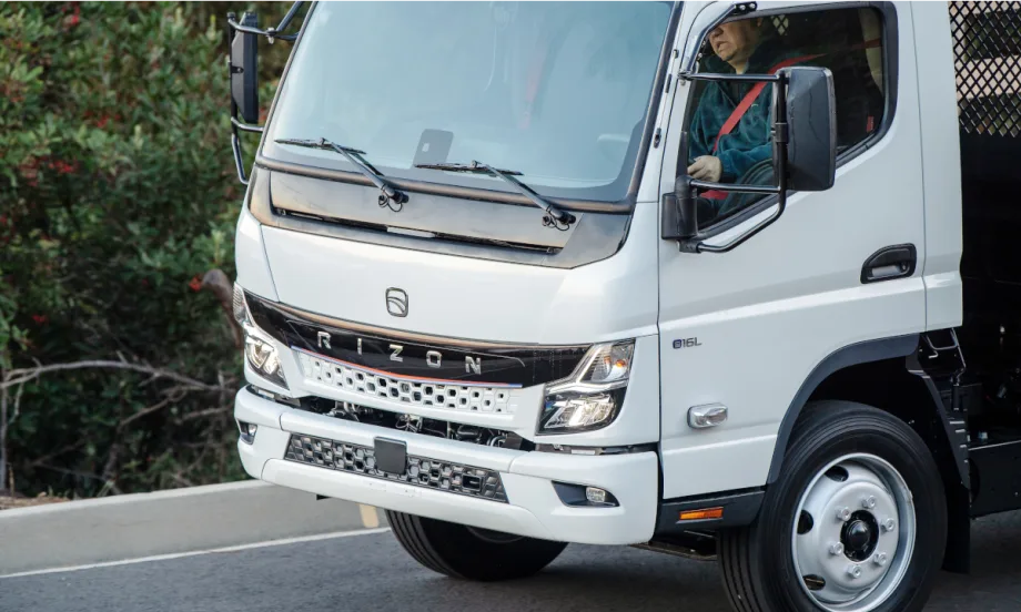 close-up photo of a man driving a white battery electric truck.