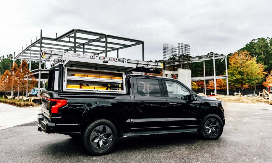 Side view of a black pickup truck with a work truck cap over bed and shelving shown in the sides.