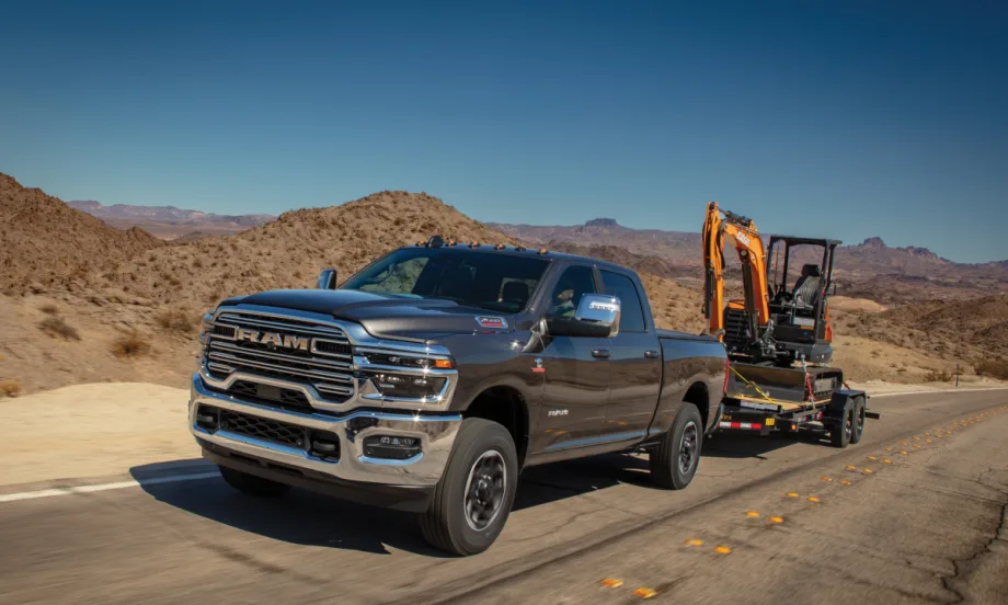 Ram HD pickup towing a mini excavator on a trailer in the desert.