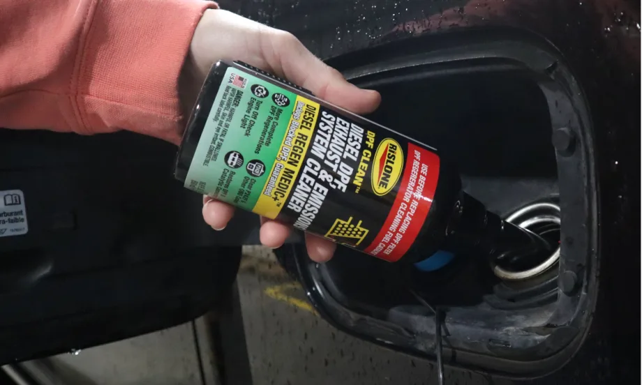 Closeup of hand touring bottle of DPF cleaner into a fuel tank.