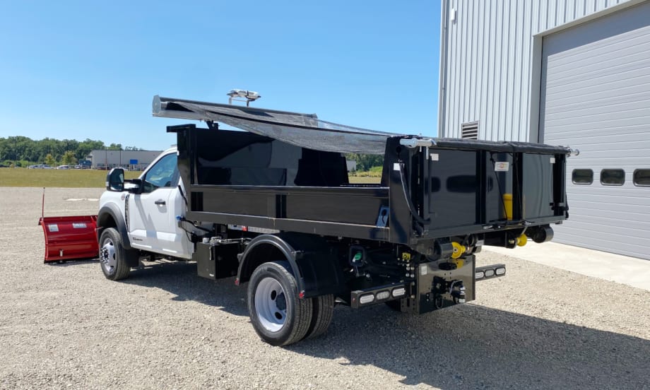 Rear quarter view of a dump body pickup with a tarping system covering the dump.
