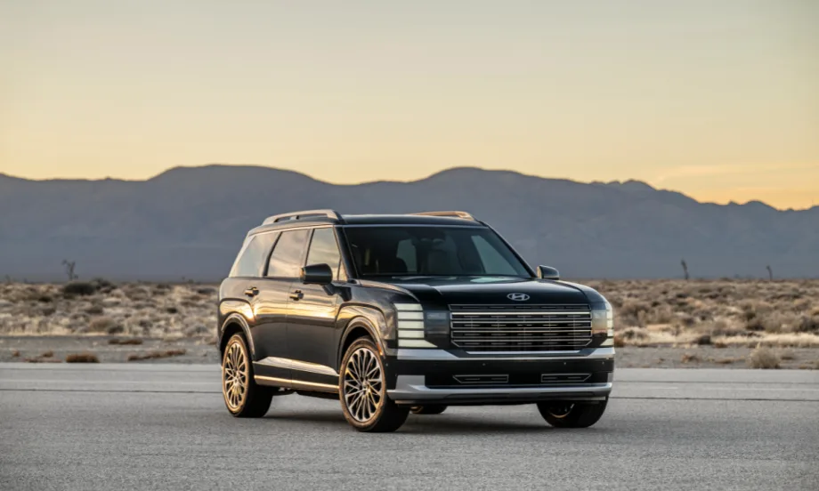 Front three-quarter view of the 2026 Hyundai Palisade SUV parked on a desert road at sunset, with mountains in the background.