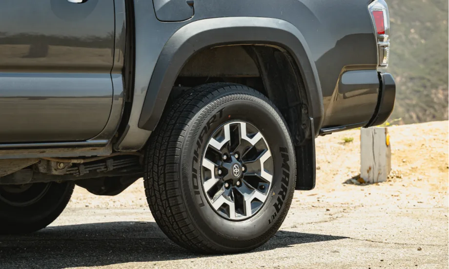 Closeup photo of the rear left tire of a pickup truck parked in a dirt area.