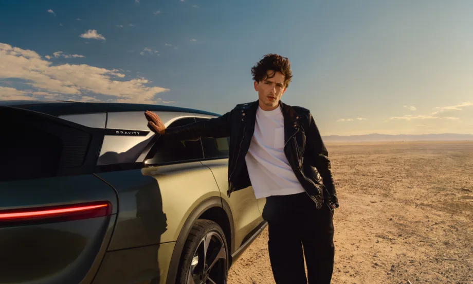 Actor Timothée Chalamet leans against a Lucid Gravity SUV in a desert setting, wearing a black leather jacket and white shirt, as part of Lucid’s new marketing campaign.