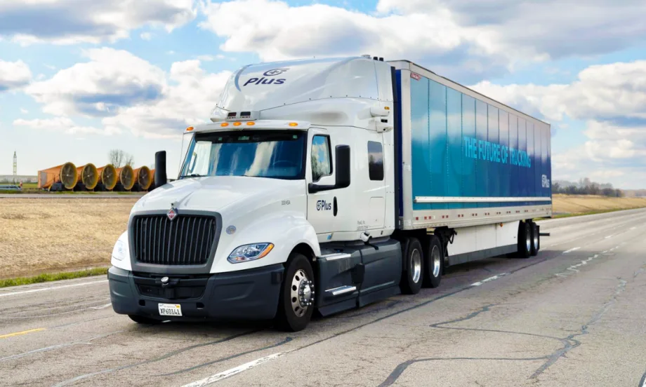 A white Plus autonomous semi-truck with a blue trailer reading "The Future of Trucking" drives on an open road under a partly cloudy sky, promoting self-driving freight technology.