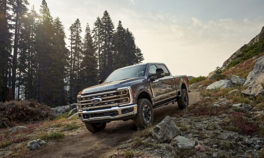 A 2026 Ford Super Duty pickup truck driving on a rocky trail in a mountainous forest setting.