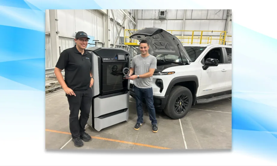 Two GM engineers stand beside a 3D printer holding a trophy, with a white Chevrolet Silverado EV Max Range Work Truck in the background and hood open after a record-setting range test.