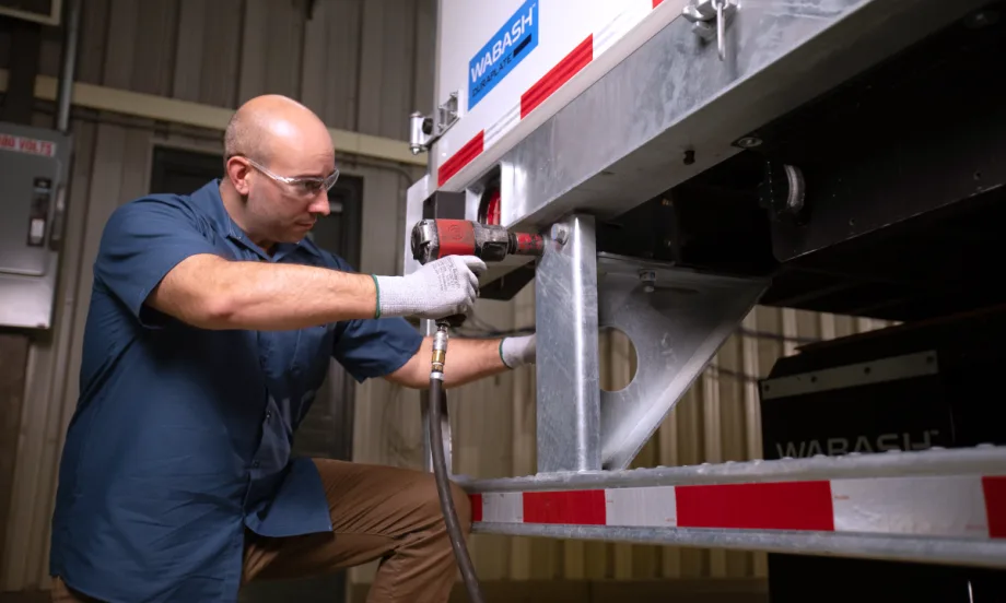 Maintenance technician working on a Wabash trailer, at the rear.