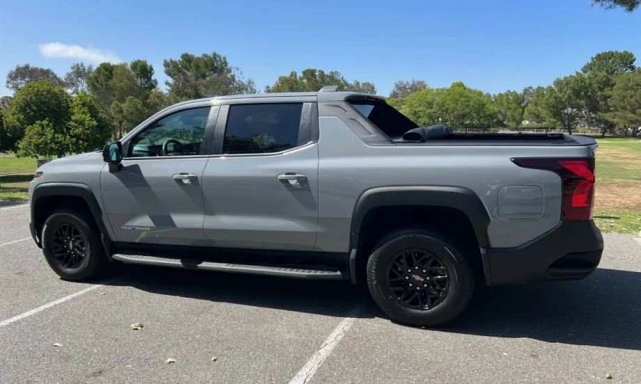 A gray Chevrolet Silverado electric pickup truck in the parking lot of a public park.