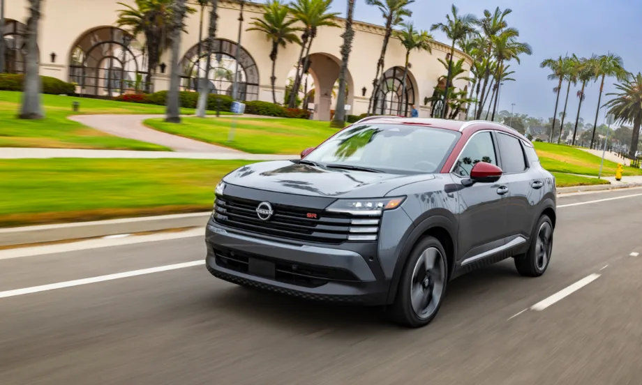 A 2026 Nissan Kicks SR in gray with red accents drives on a palm-lined street, showcasing the SUV’s updated styling and compact crossover design.