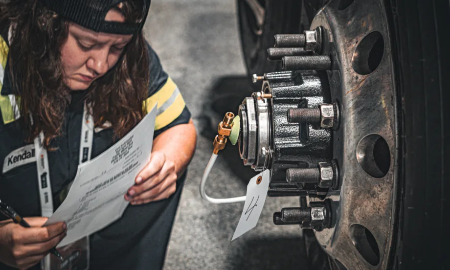 Technician reviewing paperwork while inspecting a truck wheel hub during Top Tech contest.