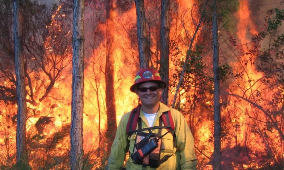 David Ronsen in firefighter gear standing in front of a raging wildfire during his early firefighting career.