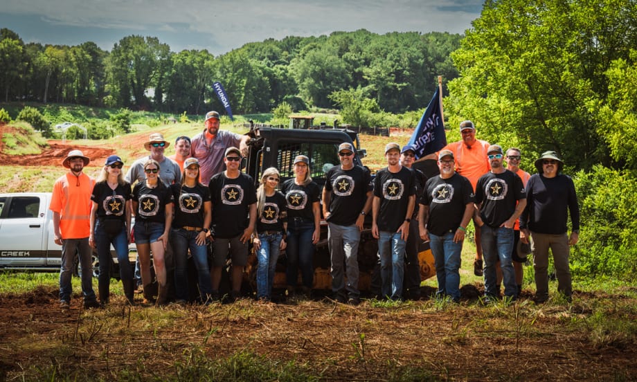 Group of National Equipment League operators and staff standing outdoors in front of equipment and trucks.