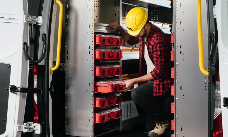 A worker in a van installing red Milwaukee Packout toolboxes into a Ranger Design Partskeeper Cabinet system.