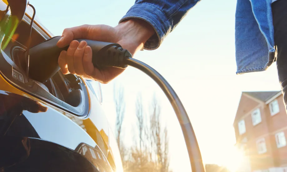 Person plugging an electric vehicle charger into a car outdoors in daylight, representing versatile charging options for different connector types.