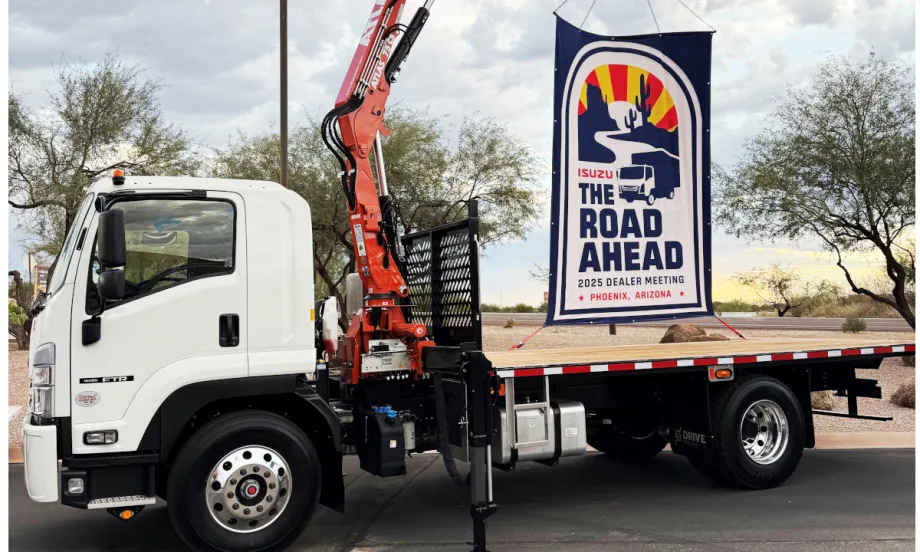 Flatbed Isuzu truck with a sign on back promoting The Road Ahead, the company's annual dealer meeting.