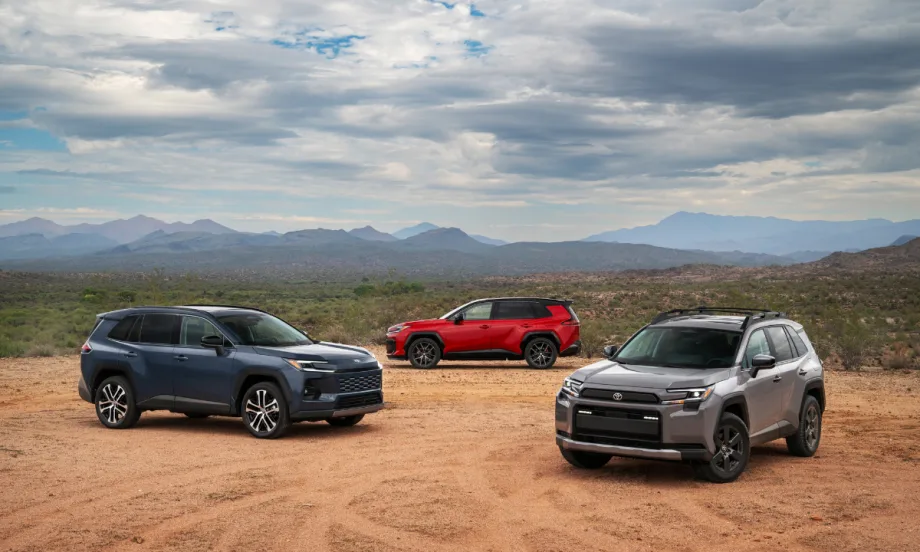 Three 2026 Toyota RAV4 SUVs—gray, red, and blue—parked in a desert landscape with mountains in the distance.
