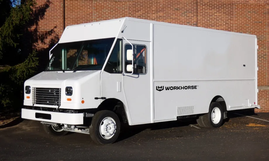 Front quarter view of a white step van parked next to the brick wall of a building.