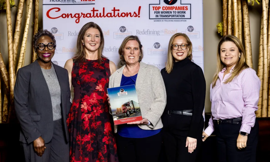 Five women stand on stage together after receiving an award.
