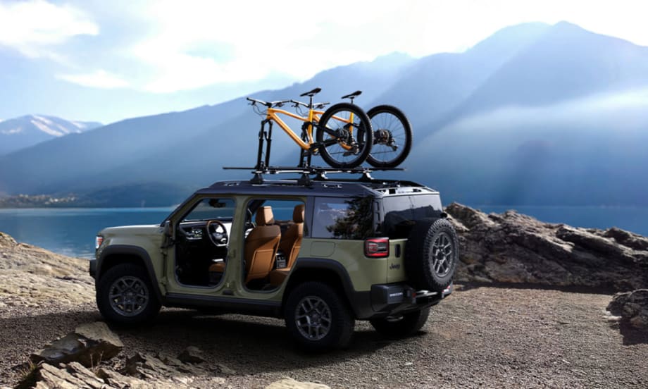 All-electric Jeep Recon SUV parked lakeside with bicycles mounted on the roof, illustrating Stellantis’ future access to Tesla Superchargers through NACS adoption.