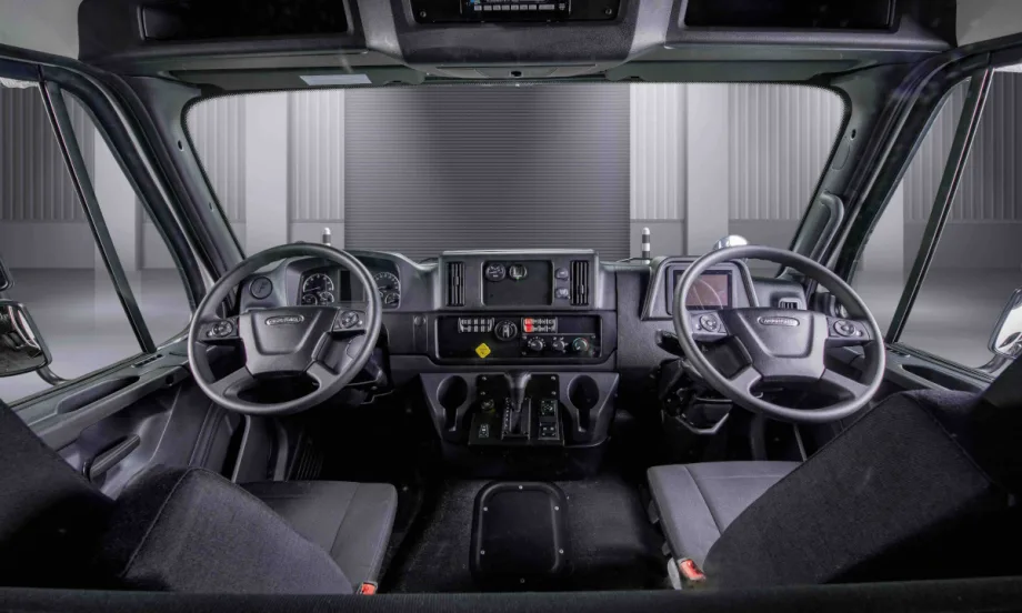 Interior view of a truck cab looking forward toward two steering wheels, one left and one right.