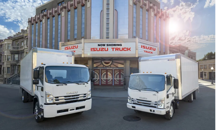 Two Isuzu box trucks parked in front of a movie theater with sign that says Now Showing, Isuzu Truck.