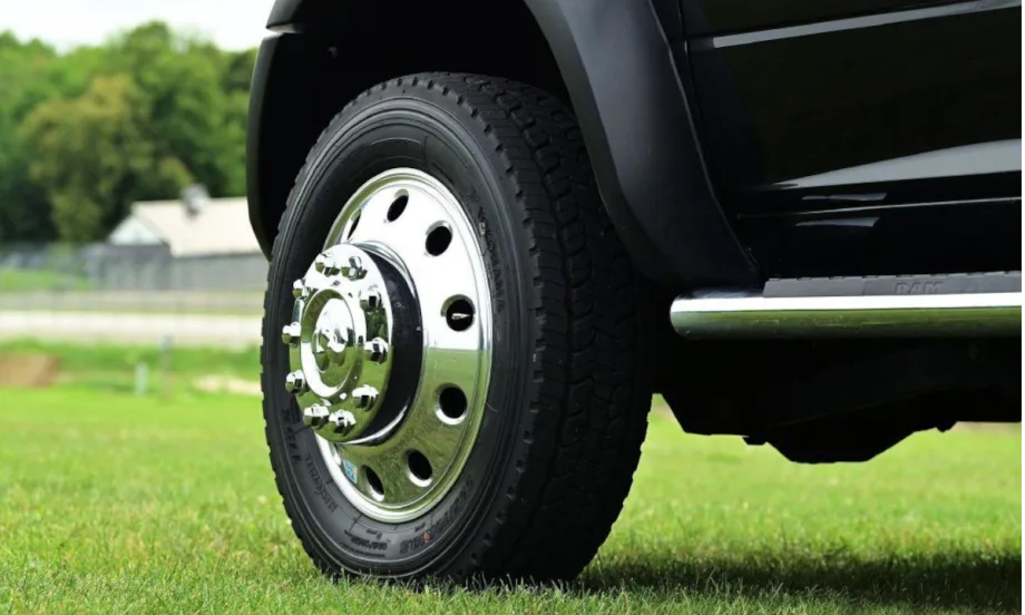 Closeup photo of a front left truck tire on a black truck parked on grass.