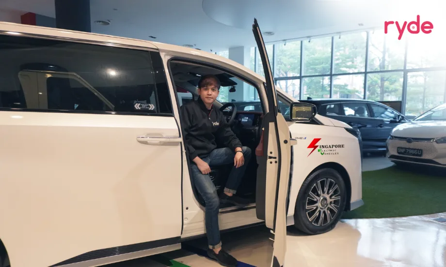 Ryde driver seated in a white electric vehicle inside a showroom, with Singapore Electric Vehicles branding on the car and other vehicles in the background.
