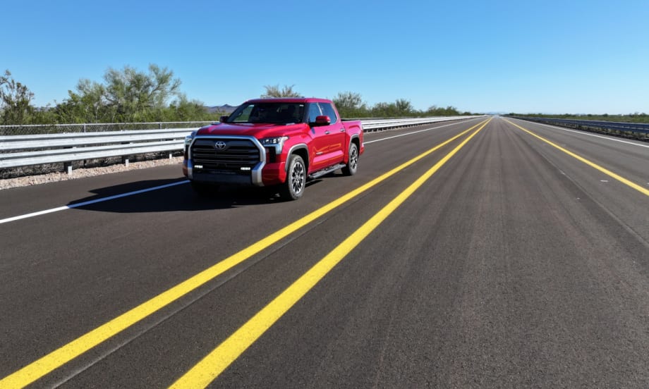 Red Toyota pickup truck driving down road with two spaced yellow lines and driving toward the camera.