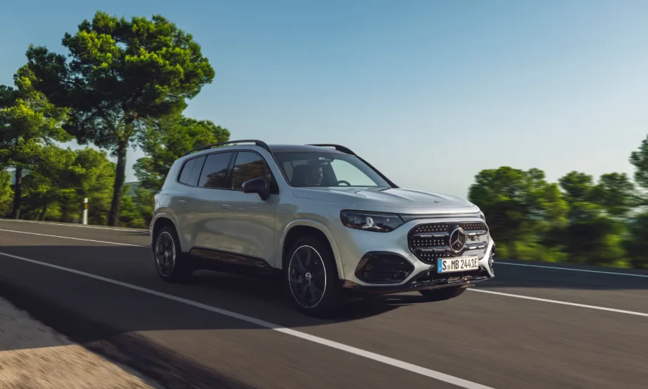 All-electric Mercedes-Benz GLB compact SUV driving on a paved road, shown in a front three-quarter view with updated exterior design and lighting.