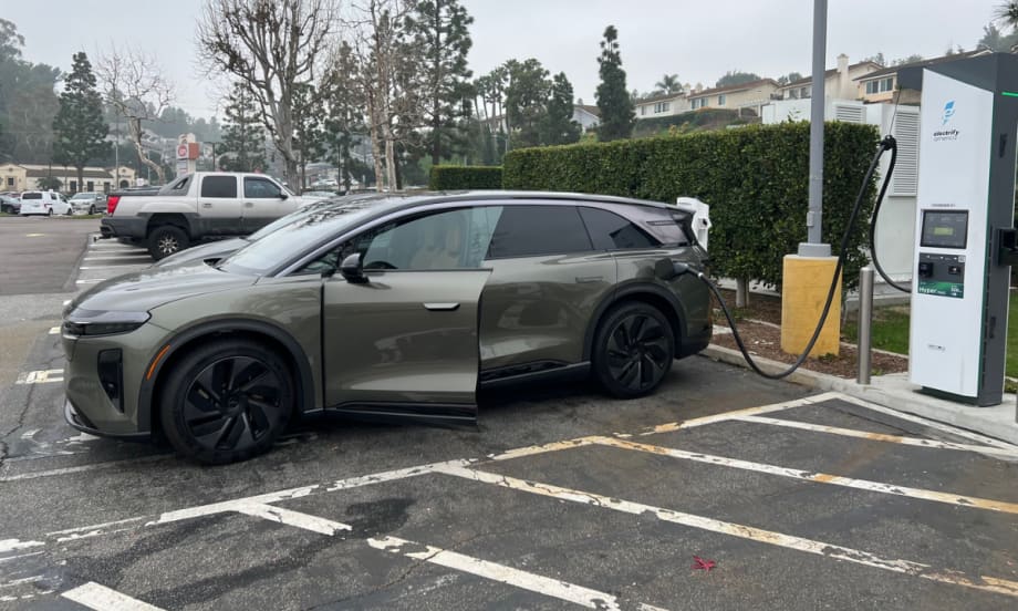 Lucid Gravity electric SUV plugged into a fast-charging station in a parking lot.